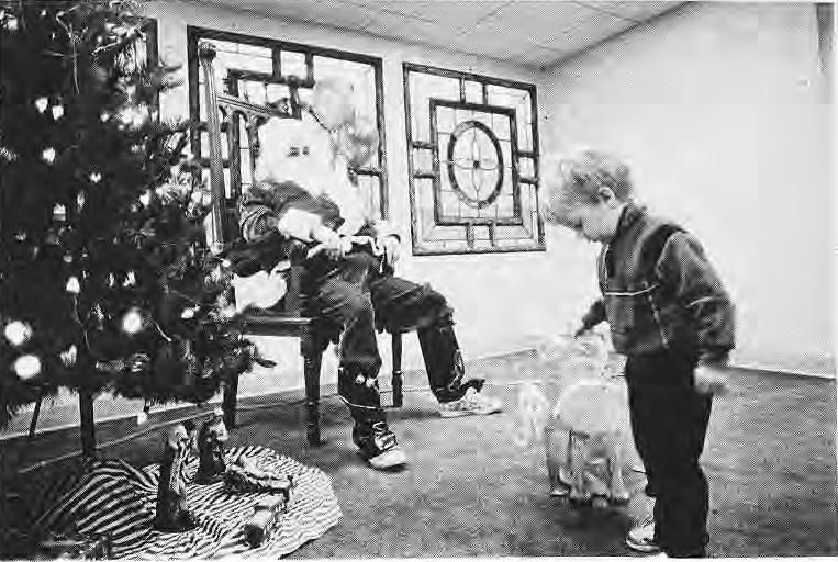 Child demonstrates a puppet to Santa, identified as Jim Merlo.
