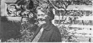 Mrs. Keiffer in her garden beside a hybrid tea rose and stone ornament, as identified in the original caption.