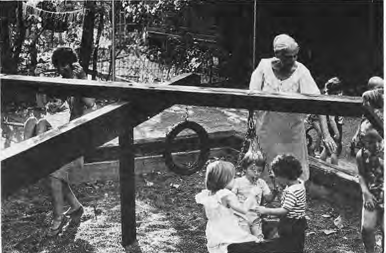 Dolores Hoefel and Betty Klinefelter playing with preschool children on new playground equipment.
