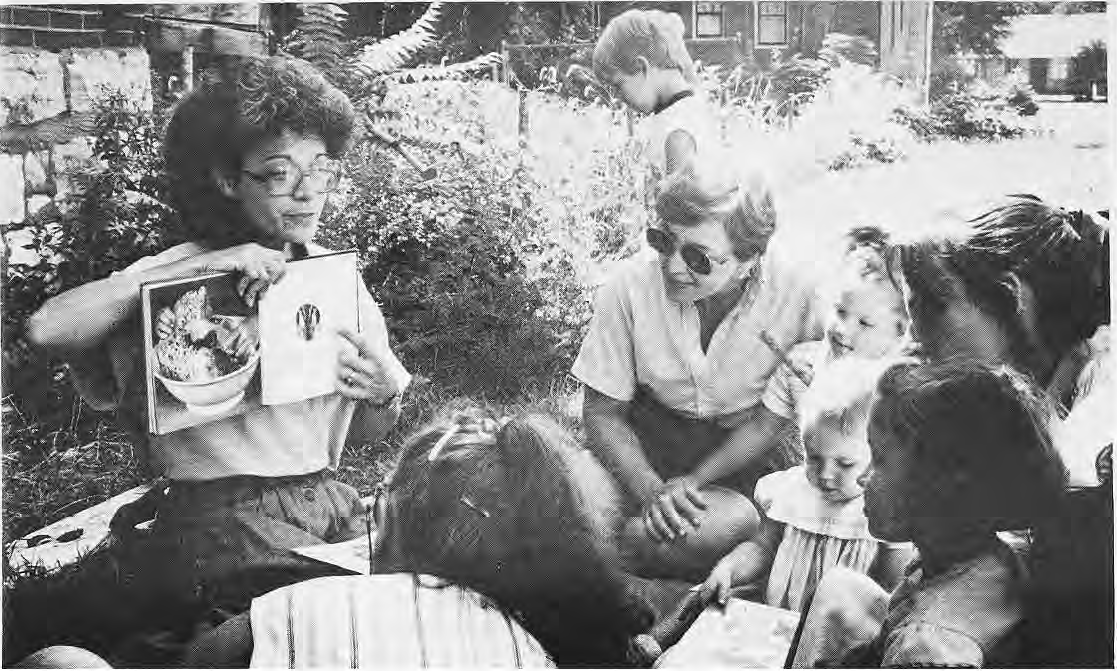 Rose Flynn sharing a picture book with children outdoors.