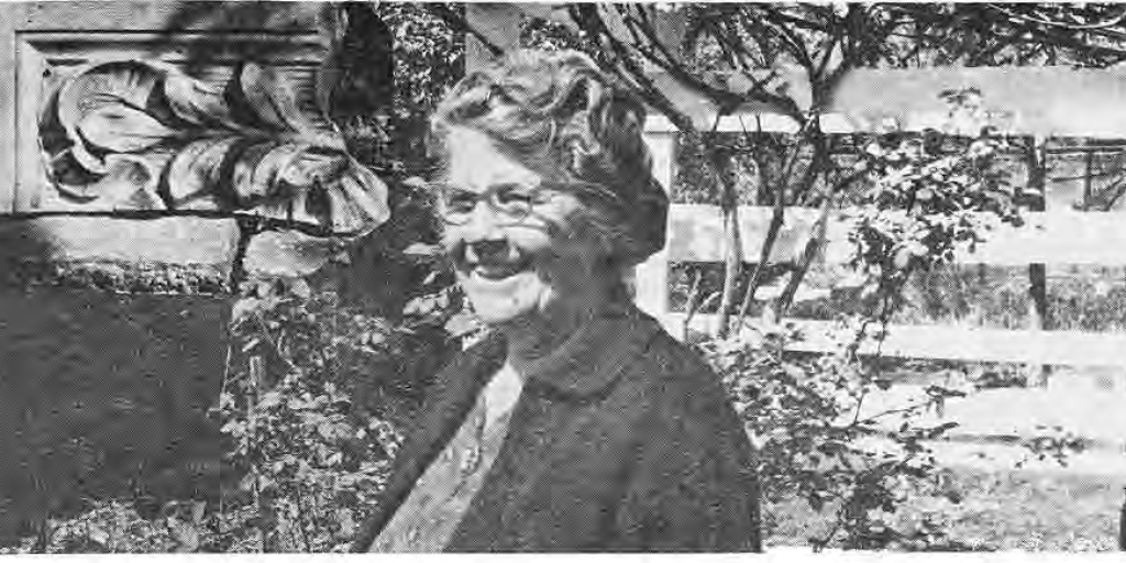 Mrs. Keiffer in her garden beside a hybrid tea rose and stone ornament, as identified in the original caption.